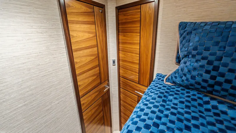 Slide: The Image of Guest Stateroom with Rich Wood Accents This image showcases the guest stateroom of the 2024 Viking 68 Convertible, featuring elegant wood cabinetry that adds warmth and sophistication. The room is complemented by luxurious, textured bedding in a deep blue hue, creating a cozy and inviting atmo - 7933142