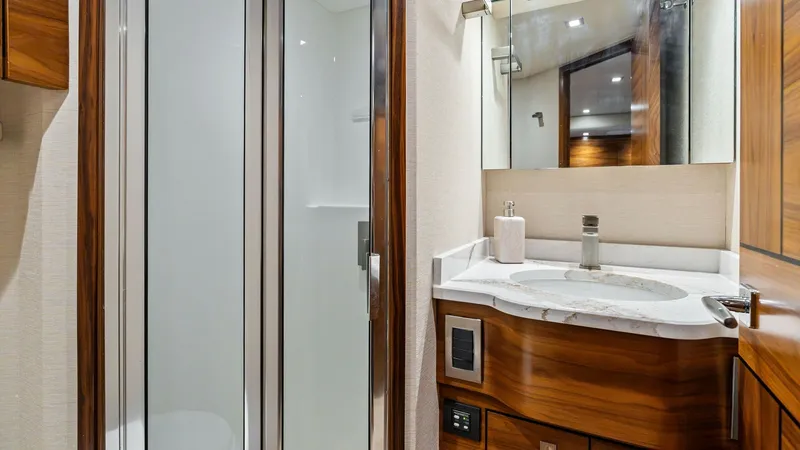 Slide: The Image of Elegant Yacht Bathroom with Shower This luxurious bathroom on the 2024 Viking 68 Convertible features a sleek glass-enclosed shower and elegant wood cabinetry. The marble countertop adds a touch of sophistication, complemented by modern fixtures and ample lighting. The space is designed fo - 7933146