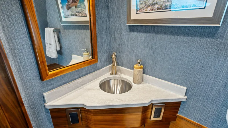 Slide: The Image of Elegant Bathroom Vanity Corner The bathroom on the 2024 Viking 68 Convertible features a sophisticated corner vanity with a sleek marble countertop and an undermount sink. Rich wood cabinetry complements the modern brushed nickel fixtures, while the textured wall covering adds a touch - 7933125
