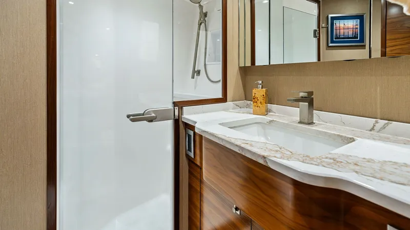 Slide: The Image of Luxurious En-Suite Bathroom This sophisticated en-suite bathroom features a stylish marble countertop and elegant wood cabinetry, adding a touch of luxury to the space. The spacious glass-enclosed shower offers a modern design with high-end fixtures. Ambient lighting and a large mir - 7933136