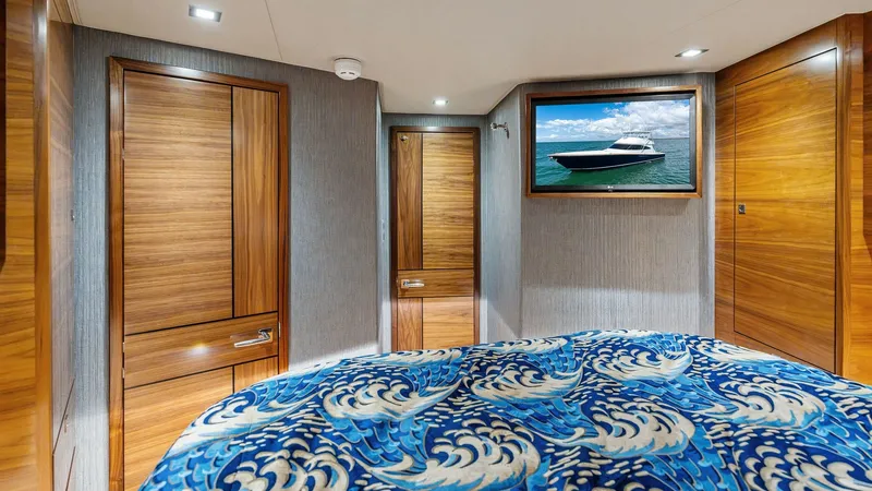 Slide: The Image of Luxurious Stateroom with Artful Decor This elegant stateroom aboard the 2024 Viking 68 Convertible features rich wood cabinetry and modern lighting, creating a warm and inviting ambiance. The bed is adorned with a vibrant, ocean-themed bedspread, adding a touch of artistic flair. A large fram - 7933138