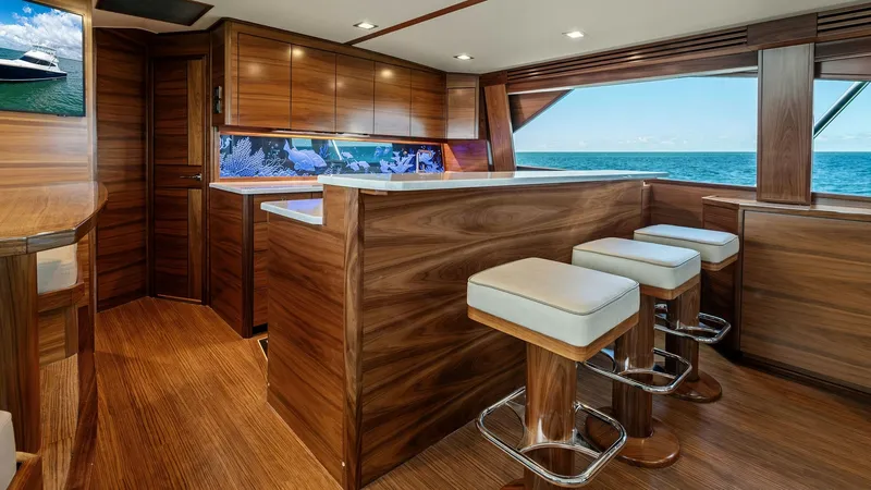 Slide: The Image of Galley and Bar Seating Area The galley on the 2024 Viking 68 Convertible features rich wood cabinetry and sleek countertops, offering a blend of functionality and style. Bar seating with plush stools provides a comfortable space for socializing, while large windows present stunning - 7933127