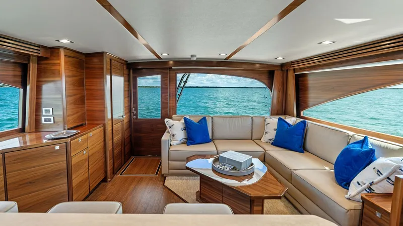 Slide: The Image of Luxurious Salon with Ocean Views The salon of the 2024 Viking 68 Convertible 'Laid Back' offers an inviting space with panoramic ocean views. Rich wooden cabinetry and plush seating adorned with vibrant blue accents create a warm, sophisticated ambiance. Large windows let in abundant nat - 7933122