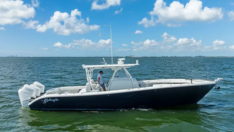 Slide: The Image of Side Profile of 39 Center Console The 2014 Yellowfin 39 Center Console is showcased in a striking side profile view on open water. Its sleek design is complemented by a robust hull and a spacious deck layout. Equipped with triple outboard engines, this model promises exceptional performan - 7943350