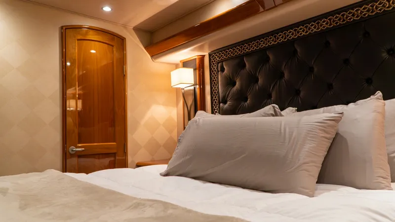 Slide: The Image of Luxurious Master Stateroom Interior The master stateroom offers a plush and inviting space with a lavishly upholstered headboard and high-quality linens. Soft ambient lighting and a warm wood finish create an elegant and relaxing atmosphere. The room's design showcases the Viking 66 Convert - 7943371