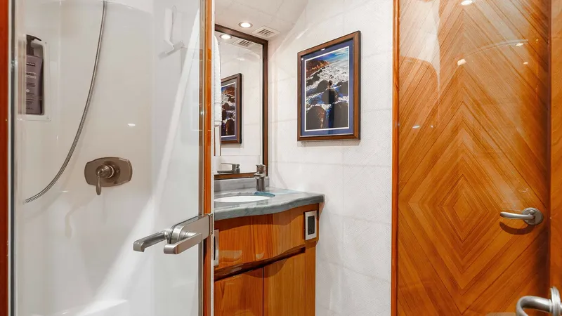 Slide: The Image of 2014 Viking 76 Enclosed Bridge "TRANQUILO" Guest Stateroom Ensuite Head This elegant ensuite bathroom features a sleek, modern shower with a glass door and high-end fixtures. The vanity area is highlighted by exquisite wood cabinetry and a stylish countertop, complemented by ambient lighting. A framed artwork adds a touch of - 7962485