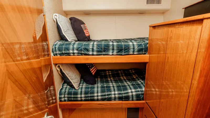 Slide: The Image of 2014 Viking 76 Enclosed Bridge "TRANQUILO" Bunk Cabin #2 This cozy guest cabin features comfortable twin bunk beds, ideal for accommodating additional guests. The warm wood finishes and plaid bedding create a welcoming atmosphere, complemented by ample storage space. The cabin's efficient layout maximizes comfo - 7962490
