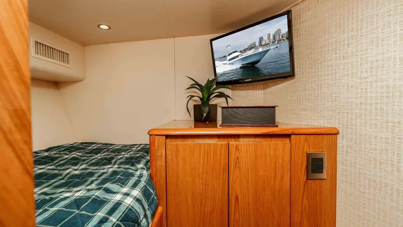 Slide: The Image of 2014 Viking 76 Enclosed Bridge "TRANQUILO" Bunk Cabin #2 This inviting guest stateroom features a comfortable bed adorned with a stylish plaid blanket. The room is equipped with a flat-screen TV mounted above a sleek wooden cabinet, providing entertainment and ample storage. Soft ambient lighting and a decorati - 7962491