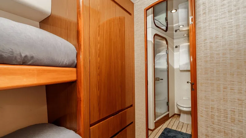 Slide: The Image of 2014 Viking 76 Enclosed Bridge "TRANQUILO" Ensuite Head Access This cozy guest stateroom on the Viking 76 Enclosed Bridge Sportfisher features comfortable twin bunk beds and warm wood cabinetry, offering ample storage. The ensuite bathroom is elegantly appointed with modern fixtures and a sleek glass shower, providin - 7962488
