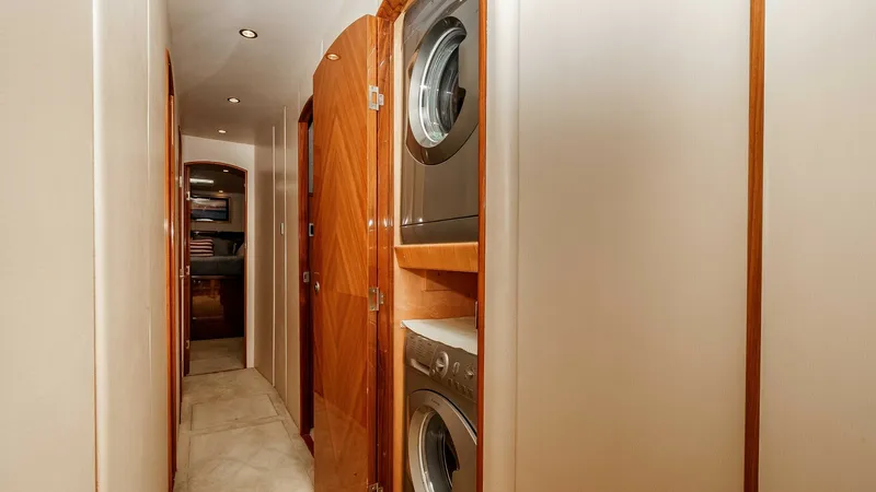 Slide: The Image of 2014 Viking 76 Enclosed Bridge "TRANQUILO" This image showcases the well-appointed hallway of the Viking 76 Enclosed Bridge Sportfisher, featuring a convenient stacked washer and dryer unit. The elegant wood paneling and soft lighting create a warm and inviting atmosphere. The design maximizes spa - 7962495