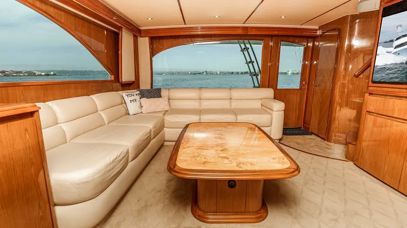 Slide: The Image of 2014 Viking 76 Enclosed Bridge "TRANQUILO" Spacious Salon with Aft Access to the Cockpit Highlighting the spacious salon aboard the 2014 Viking Enclosed Bridge; featuring a large L-shaped cream leather sofa and custom teak coffee table with a beautifully finished burlwood-style top. Rich teak cabinetry and trim throughout complement the light - 7962464
