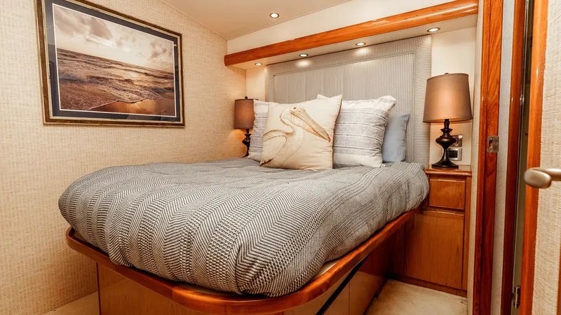 Slide: The Image of 2014 Viking 76 Enclosed Bridge "TRANQUILO" Guest Stateroom This inviting guest stateroom features a comfortable double bed adorned with plush bedding and decorative pillows. The warm wooden cabinetry and soft lighting create a cozy and elegant atmosphere, perfect for relaxation. A beautifully framed seascape pain - 7962483