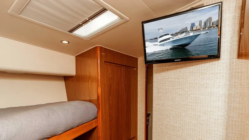Slide: The Image of 2014 Viking 76 Enclosed Bridge "TRANQUILO" This cozy guest cabin features a comfortable bunk bed with plush bedding, perfect for relaxing after a day at sea. The space is enhanced by a wall-mounted flat-screen TV, offering entertainment options for guests. The tasteful wood finishes and soft light - 7962487