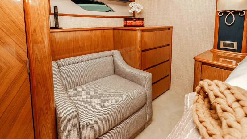 Slide: The Image of 2014 Viking 76 Enclosed Bridge "TRANQUILO" Master Stateroom Lounge Chair This cozy Master Stateroom features a comfortable lounge chair complemented by rich wood cabinetry, offering ample storage space. The soft lighting and elegant fabric wall coverings create a warm, inviting ambiance. A large window adds natural light, enha - 7962479
