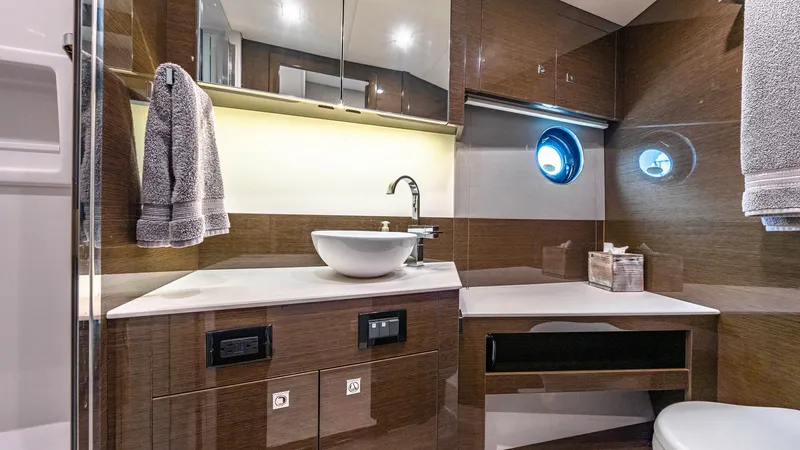 Slide: The Image of Luxurious Ensuite Bathroom The ensuite bathroom on the Serenity features elegant wood cabinetry and a sleek vessel sink, exuding modern sophistication. LED lighting under the cabinets enhances the ambient atmosphere, while the porthole provides natural light and a nautical touch. H - 8141253