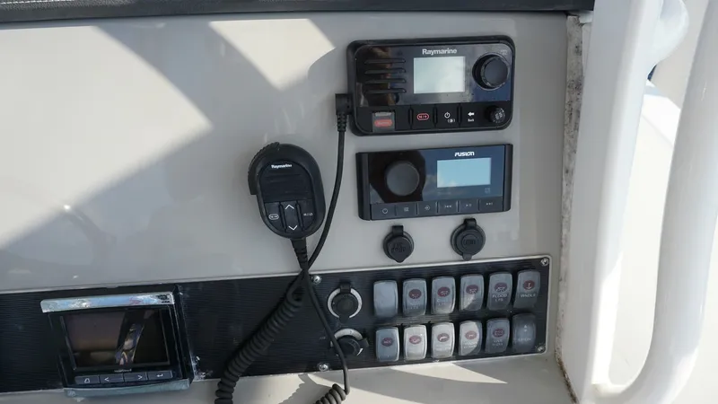 Slide: The Image of Helm Console with Electronics Panel This image showcases the helm console of the 2016 Boston Whaler 270 Dauntless, featuring a well-organized electronics panel. Equipped with state-of-the-art Raymarine and Fusion systems, it ensures reliable navigation and communication. The neatly arranged - 8087567