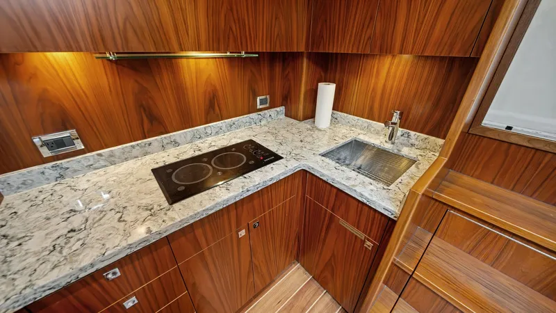 Slide: The Image of Galley with Marble Countertops The galley of the 2017 Hatteras GT45X features elegant marble countertops and rich wooden cabinetry, creating a luxurious and functional space. Equipped with a modern two-burner cooktop and a sleek sink, this area offers all the amenities needed for gourm - 8439527