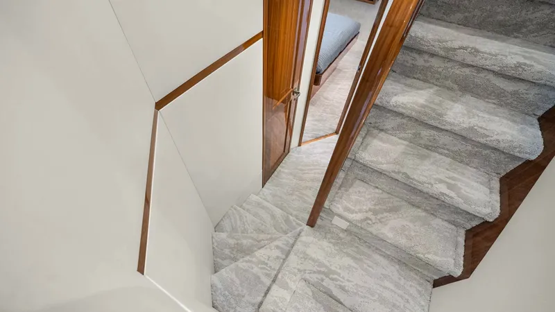 Slide: The Image of Carpeted Staircase to Lower Deck This elegant staircase on the Viking 92 Enclosed Bridge features plush carpeting for comfort and safety. The warm wooden accents provide a touch of luxury, seamlessly integrating with the vessel's sophisticated interior. The stairs lead to the lower deck, - 8439601