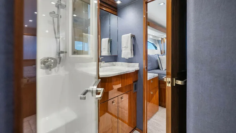 Slide: The Image of Guest Ensuite with Shower and Vanity The guest ensuite on the Viking 92 Enclosed Bridge features a sleek, modern shower with glass door and chrome fixtures. The vanity is elegantly designed with high-gloss wood cabinetry and a polished countertop, offering ample space and storage. Soft light - 8439604