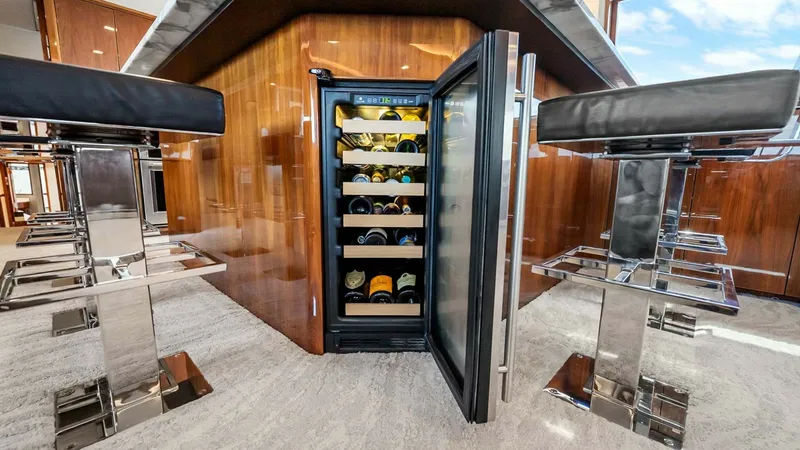 Slide: The Image of Luxury Bar Area with Wine Cooler The sleek bar area on the Viking 92 Enclosed Bridge features a high-end wine cooler, elegantly integrated into the rich wood cabinetry. The polished flooring and plush bar stools enhance the luxurious ambiance, providing a perfect setting for entertaining - 8439580