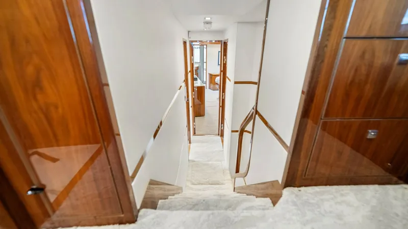 Slide: The Image of Luxurious Interior Staircase This image showcases the elegant interior staircase of the Viking 92 Enclosed Bridge. The stairway features rich wood paneling complemented by plush carpeting, leading to the main living areas. The craftsmanship and attention to detail are evident, creati - 8439612