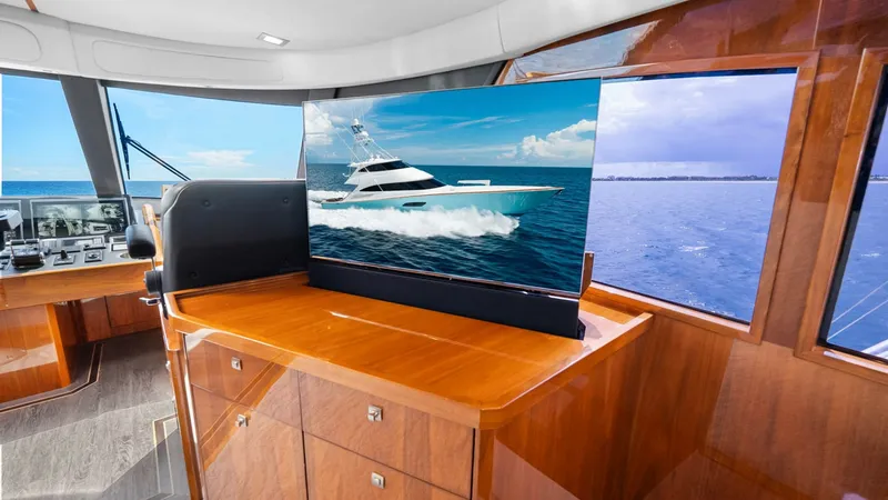 Slide: The Image of Enclosed Bridge Helm with TV Display The enclosed bridge of the 2017 Viking 92 Enclosed Bridge features a sleek helm station with state-of-the-art navigation equipment. Highlighted is a retractable flat-screen TV, seamlessly integrated into the rich wood cabinetry, offering both entertainmen - 8439590