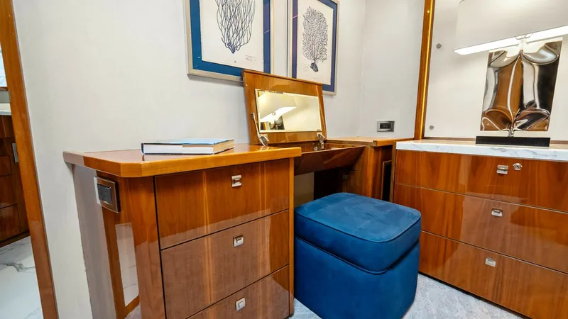 Slide: The Image of Elegant Vanity Area This luxurious vanity area on the Viking 92 Enclosed Bridge features exquisite wood cabinetry with sleek, modern hardware. A plush, deep blue ottoman complements the warm wood tones, providing a comfortable seating option. The space is elegantly accented - 8439615