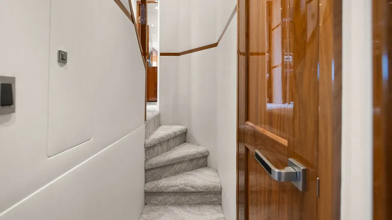 Slide: The Image of Elegant Stairway with Wooden Accents This image showcases the elegant stairway of the 2017 Viking 92 Enclosed Bridge, featuring plush carpeting that adds a touch of luxury to the space. The beautifully crafted wooden accents and trim provide a warm, sophisticated ambiance. The seamless integ - 8439600