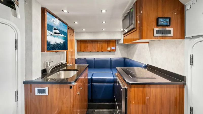 Slide: The Image of Galley and Dinette Area This image reveals the elegant galley and dinette area of the Viking 92 Enclosed Bridge, showcasing sleek wooden cabinetry and polished countertops. The compact yet efficient layout features a modern induction cooktop, stainless steel sink, and built-in m - 8439626