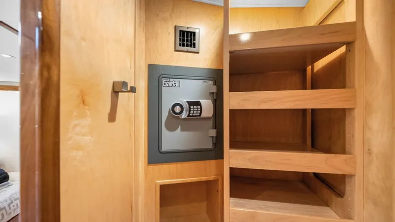 Slide: The Image of Secure Storage Compartment with Safe This image showcases a secure storage area within the Viking 92 Enclosed Bridge, featuring a built-in safe for valuables. The space is elegantly designed with high-quality wood finishes and multiple shelves for organized storage. The addition of recessed - 8439622