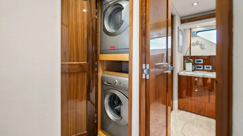 Slide: The Image of Laundry Area with Washer and Dryer This image showcases the convenient laundry area on the Viking 92 Enclosed Bridge, featuring a stacked washer and dryer set neatly enclosed in a wooden cabinet. The high-gloss wood finish adds a touch of elegance, seamlessly integrating the utility space - 8439611