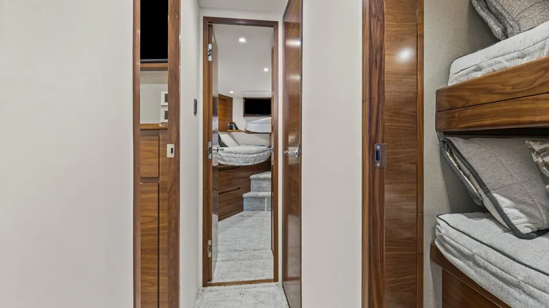 Slide: The Image of Hallway Leading to Forward Stateroom This image showcases the elegant hallway of the 2024 Viking 54 Convertible, leading to the forward stateroom. The high-gloss wood finishes and soft carpeting create a warm and inviting atmosphere, complemented by recessed lighting overhead. On the right, - 8439787