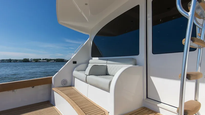 Slide: The Image of Aft Deck Seating Area This image showcases the elegant aft deck of the 2024 Viking 54 Convertible, featuring a plush seating area perfect for relaxation. The teak decking complements the sleek white finishes, creating a luxurious outdoor space. Large windows provide ample natu - 8439805
