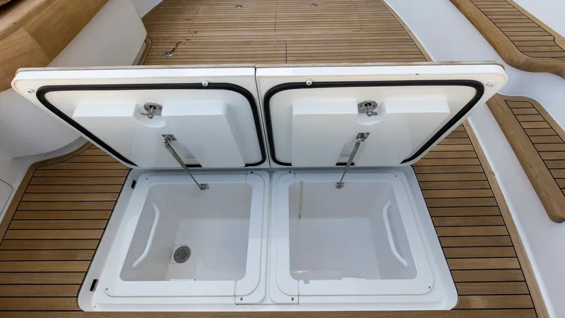 Slide: The Image of Cockpit Deck with Storage Hatches This image showcases the cockpit area of the 2024 Viking Nomad 54 Convertible, featuring dual storage hatches seamlessly integrated into the teak deck. The hatches are equipped with gas-assist struts for easy access and secure closure. The elegant teak fi - 8439809