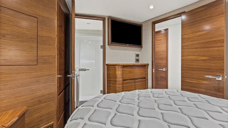 Slide: The Image of Master Stateroom with En Suite Bathroom The master stateroom of the 2024 Viking Nomad 54 Convertible features elegant wood finishes and a plush, patterned bedspread for ultimate comfort. A flat-screen TV is mounted above a sleek dresser, providing entertainment and ample storage. The room offer - 8439790