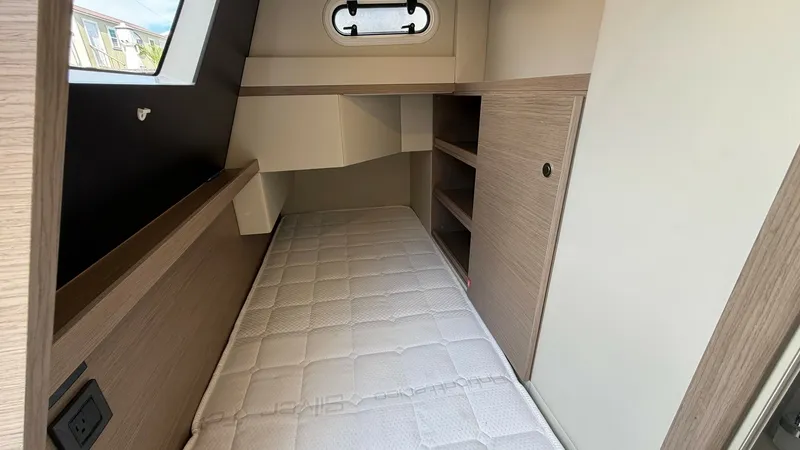 Slide: The Image of Cozy Guest Cabin with Storage This guest cabin on the 2026 Absolute Navetta 58 features a comfortable single berth with elegant wood finishes. Ample storage is provided by built-in shelving and a cabinet, ensuring convenience for extended voyages. A porthole allows natural light to il - 8640156
