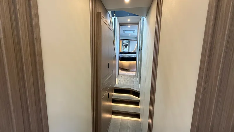 Slide: The Image of Corridor Leading to Master Stateroom This image showcases a sleek corridor leading to the master stateroom on the Absolute Navetta 58. The hallway features elegant wood paneling and soft overhead lighting, creating a warm and inviting atmosphere. The steps provide a gentle transition to the - 8640136