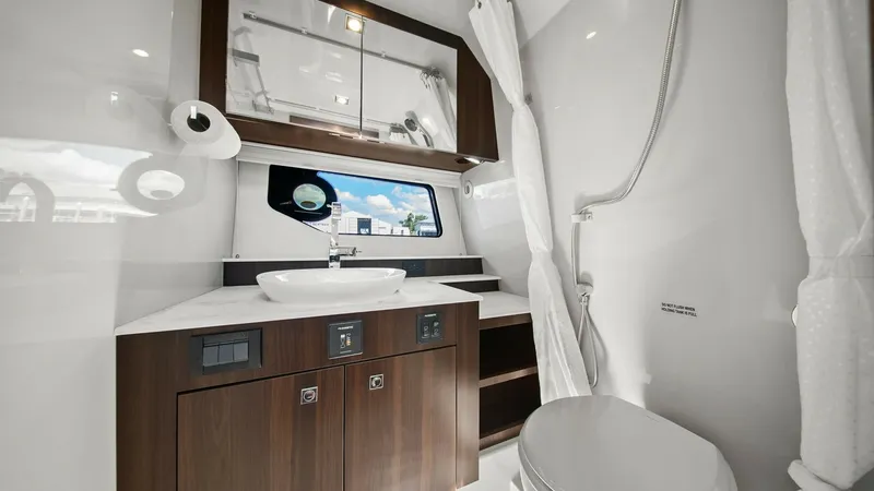 Slide: The Image of Elegant Bathroom with Vanity This modern bathroom on the 2023 Cruisers Yachts 42 GLS features a sleek vanity with a stylish vessel sink and rich wood cabinetry. The space is enhanced by a polished mirror and a practical porthole window, offering natural light and a view of the outdoo - 8619157