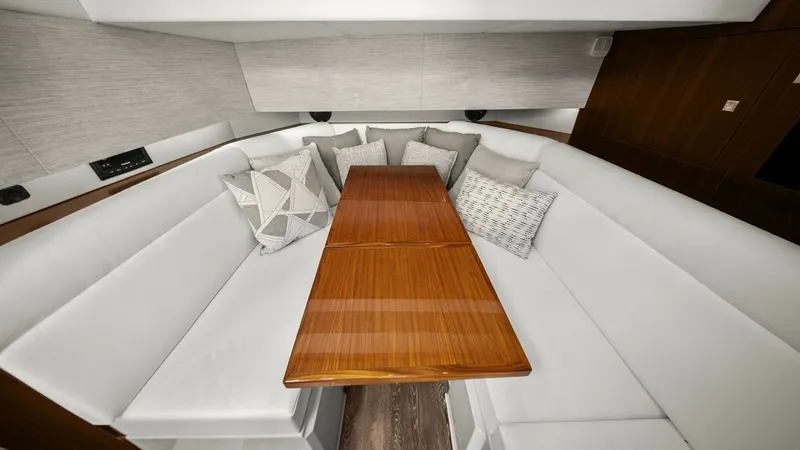 Slide: The Image of Spacious Interior Lounge Area The 2023 Cruisers Yachts 42 GLS features a luxurious interior lounge with plush, white seating that wraps around a polished wooden table. The space is accentuated by plush throw pillows and elegant wood finishes, creating a comfortable and stylish environ - 8619155