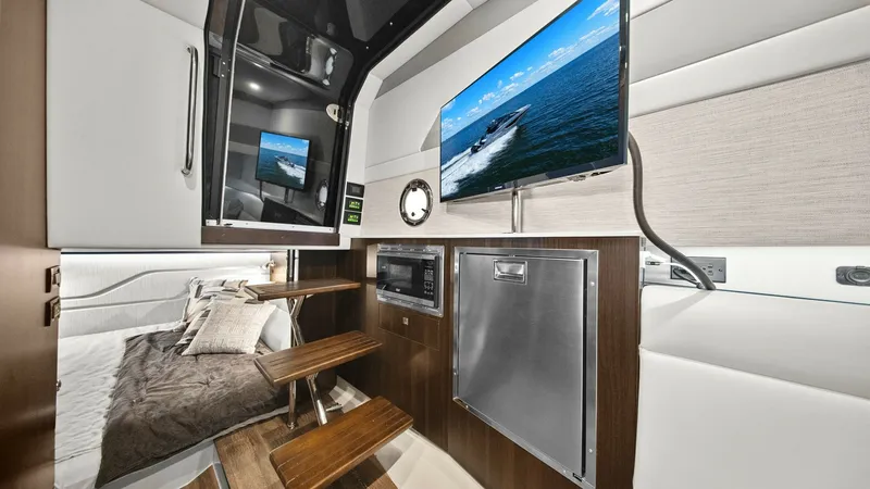 Slide: The Image of Lower Deck Entertainment and Sleeping Area This area of the 2023 Cruisers Yachts 42 GLS features a sleek entertainment setup with a wall-mounted TV and integrated sound system, ideal for relaxation. The contemporary design includes elegant wood finishes and a compact kitchenette with a microwave. - 8619156