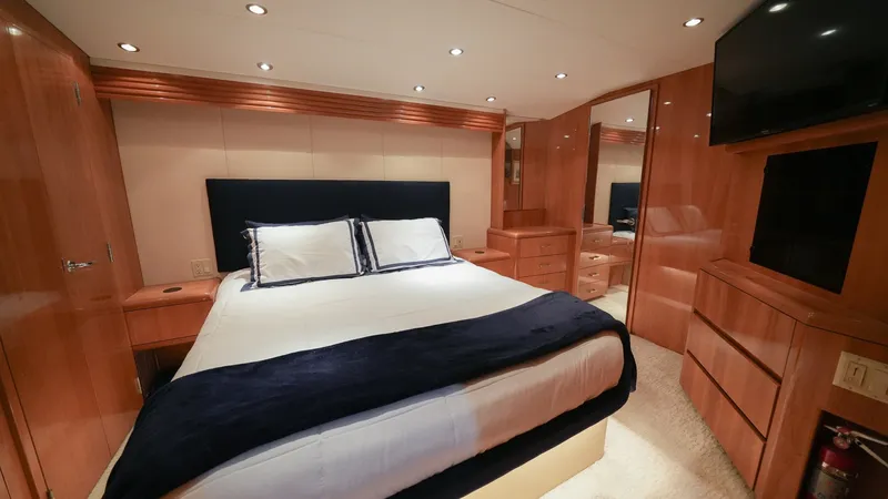 Slide: The Image of Master Stateroom with Queen Bed The master stateroom on the 2001 Hatteras 60 Convertible boasts a luxurious queen bed, accented by rich wood finishes and ample storage. The space is elegantly lit with recessed lighting, enhancing the warm tones of the cabinetry. A large mirror and a wal - 8734336
