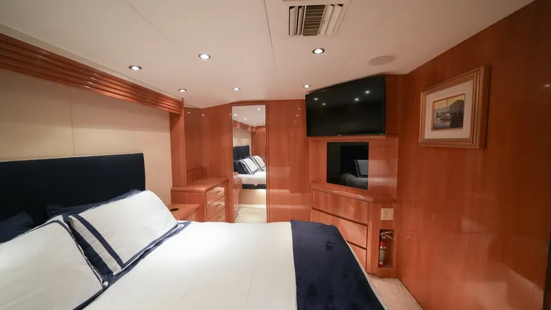 Slide: The Image of Master Stateroom with Luxurious Finish The master stateroom aboard the 2001 Hatteras 60 Convertible, Uno Mas, features rich wood paneling and elegant finishes. A plush queen-sized bed with crisp linens is complemented by ambient recessed lighting, creating a warm and inviting atmosphere. The r - 8734337