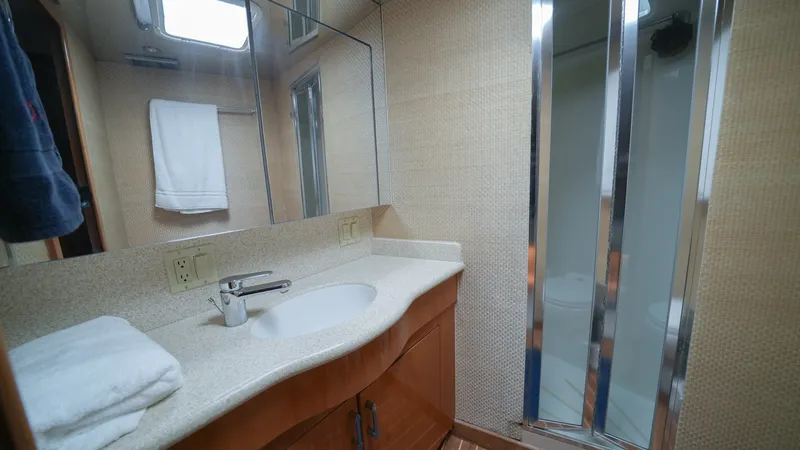 Slide: The Image of Elegant Guest Bathroom with Shower This well-appointed guest bathroom on the 2001 Hatteras 60 Convertible features a sleek countertop with an integrated sink and modern faucet. The space is enhanced by a mirrored wall and ample natural light from the overhead hatch. A stylish sliding door - 8734335