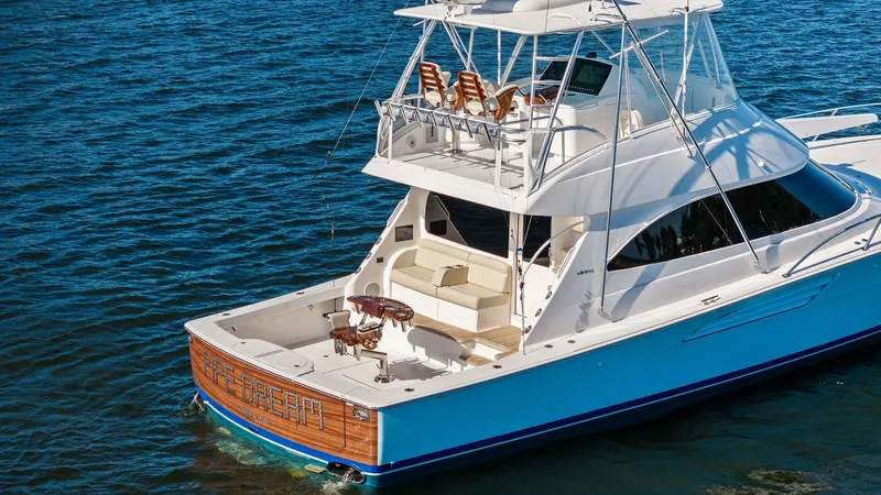 Slide: The Image of Aft Deck and Flybridge View This image showcases the aft deck and flybridge of the 2021 Viking 54 Convertible, 'Pipe Dream.' The spacious aft deck features a high-quality fighting chair and ample seating, ideal for fishing enthusiasts. The flybridge offers comfortable seating with a - 8673353