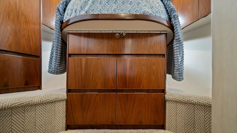 Slide: The Image of Forward Stateroom with Storage The forward stateroom of the 2021 Viking 54 Convertible features elegant wood cabinetry with ample storage beneath the bed. The plush carpeting complements the rich wood finishes, providing a warm and inviting atmosphere. Overhead lighting enhances the co - 8673317