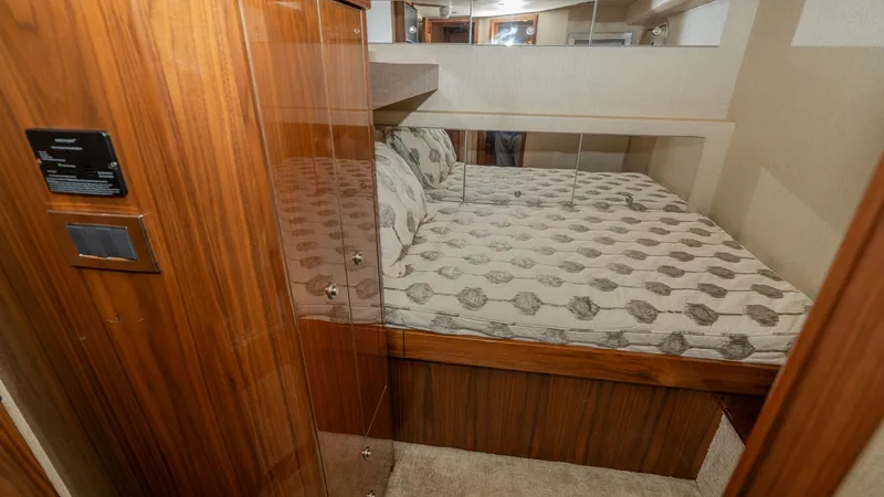 Slide: The Image of Guest Stateroom with Storage This guest stateroom on the 2019 Viking 68 Enclosed Bridge features a cozy berth with elegant patterned bedding. The room is accentuated by rich wood cabinetry offering ample storage. Mirrored accents enhance the sense of space, while soft lighting create - 8738040