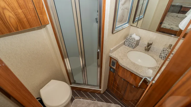 Slide: The Image of En-Suite Bathroom with Shower This elegant en-suite bathroom on the 2019 Viking 68 Enclosed Bridge features a sleek glass-enclosed shower and contemporary fixtures. The space is adorned with rich wood cabinetry and a polished stone countertop, creating a luxurious and practical enviro - 8738041