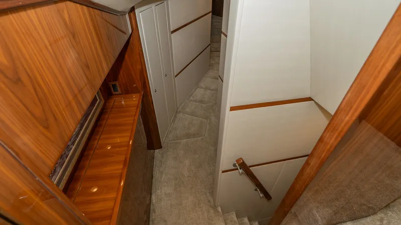Slide: The Image of Lower Deck Corridor and Staircase This image showcases the elegant corridor leading to the lower deck of the 2019 Viking 68 Enclosed Bridge. The hallway features luxurious wood paneling and plush carpeting, creating a warm and inviting atmosphere. The well-lit staircase is complemented by - 8738037