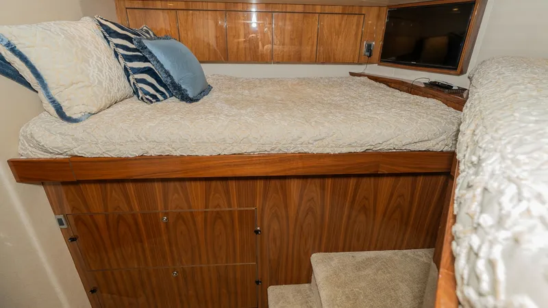 Slide: The Image of Guest Stateroom with Elevated Berth This guest stateroom features an elevated berth with plush bedding and stylish accent pillows, providing a cozy retreat. The warm wood cabinetry offers ample storage, while soft carpeting enhances comfort. Recessed lighting and a mounted TV add to the lux - 8738044