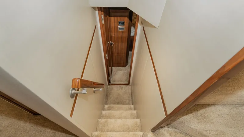 Slide: The Image of Interior Staircase to Lower Deck This image showcases the elegant staircase leading to the lower deck of the 2019 Viking 68 Enclosed Bridge, Sandman. The stairway features plush carpeting, enhancing comfort and safety, while the polished wood handrail adds a touch of sophistication. The - 8738039